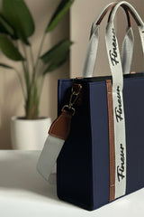 Navy Blue Tote with a white strap featuring 'fineur' branding, placed on a surface with a plant in the background.