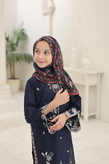 Young girl wearing a navy blue traditional outfit with a patterned hijab indoors.