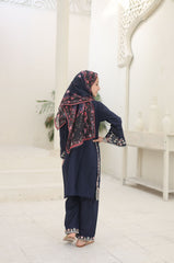 Woman in a navy blue traditional outfit with a floral headscarf in a white room.