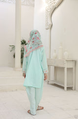 Person wearing a light blue traditional outfit with a floral headscarf in a white room.