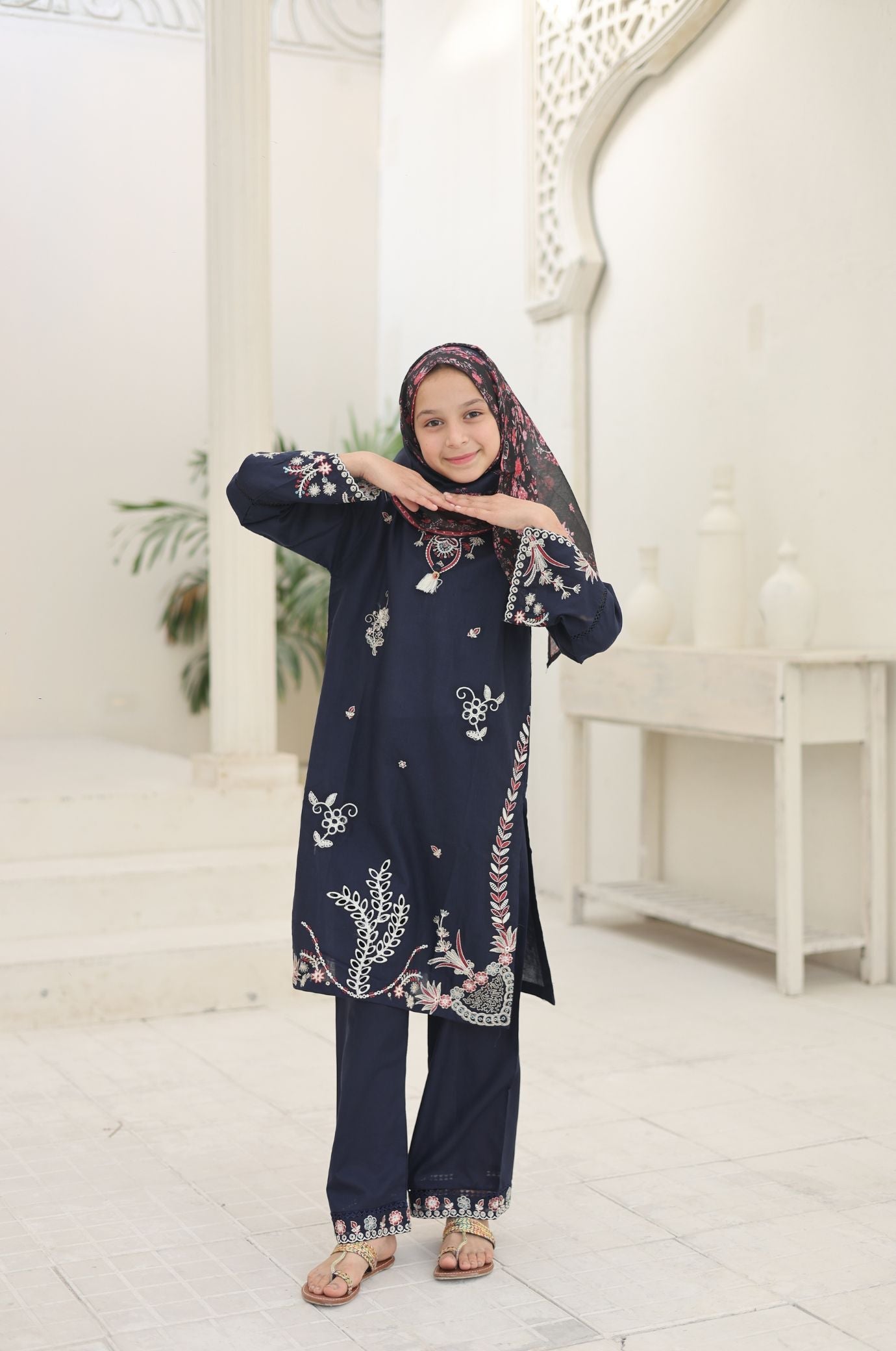 Person wearing a navy blue embroidered outfit in a white room