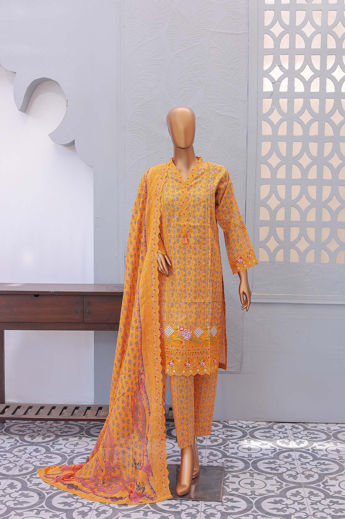 A festive embroidered three-piece outfit in gold color with embroidered front and sleeves, and a printed dupatta.