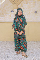 Child wearing a floral outfit standing on a textured surface with a beige wall in the background