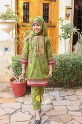 Child wearing a green and pink traditional outfit standing outdoors.