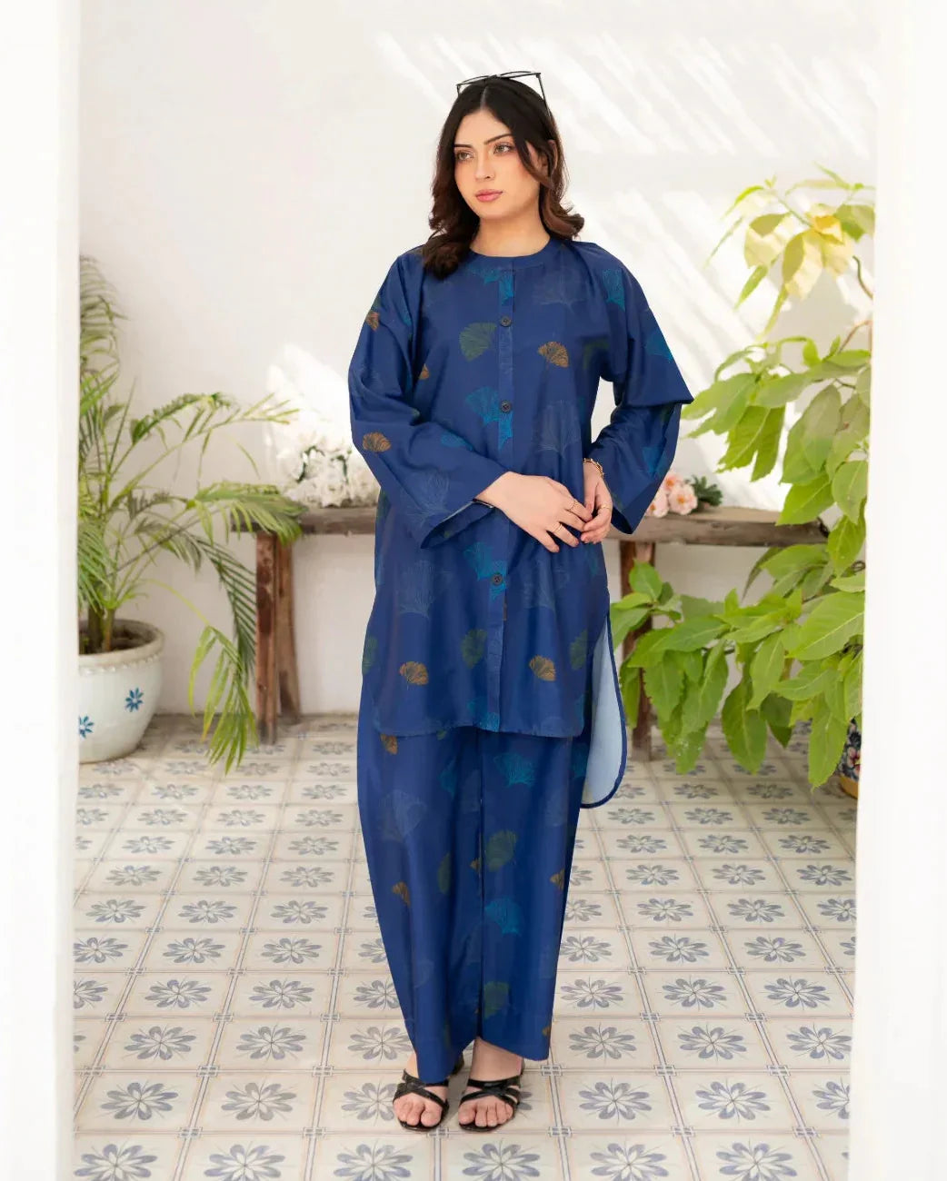 Woman wearing a navy blue traditional printed in a room with plants and a tiled floor.