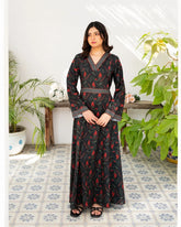 Woman wearing a black printed dress standing in a room with plants and a tiled floor.
