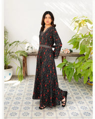 Woman wearing a black dress with floral print in a room with plants and a wooden table.