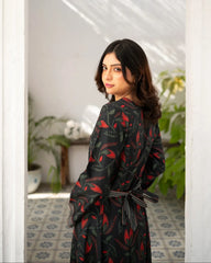 Woman wearing a black printed dress in a room with plants and a mirror.