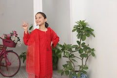 Young girl in a red outfit standing indoors with plants and a pink bicycle in the background