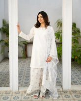 Woman in a white traditional kurta set standing in a room with white walls and tiled floor.