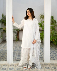 Woman in a white traditional kurta set standing in a room with white walls and tiled floor.