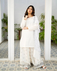 Woman in a white traditional kurta set standing in a decorative interior setting with plants.