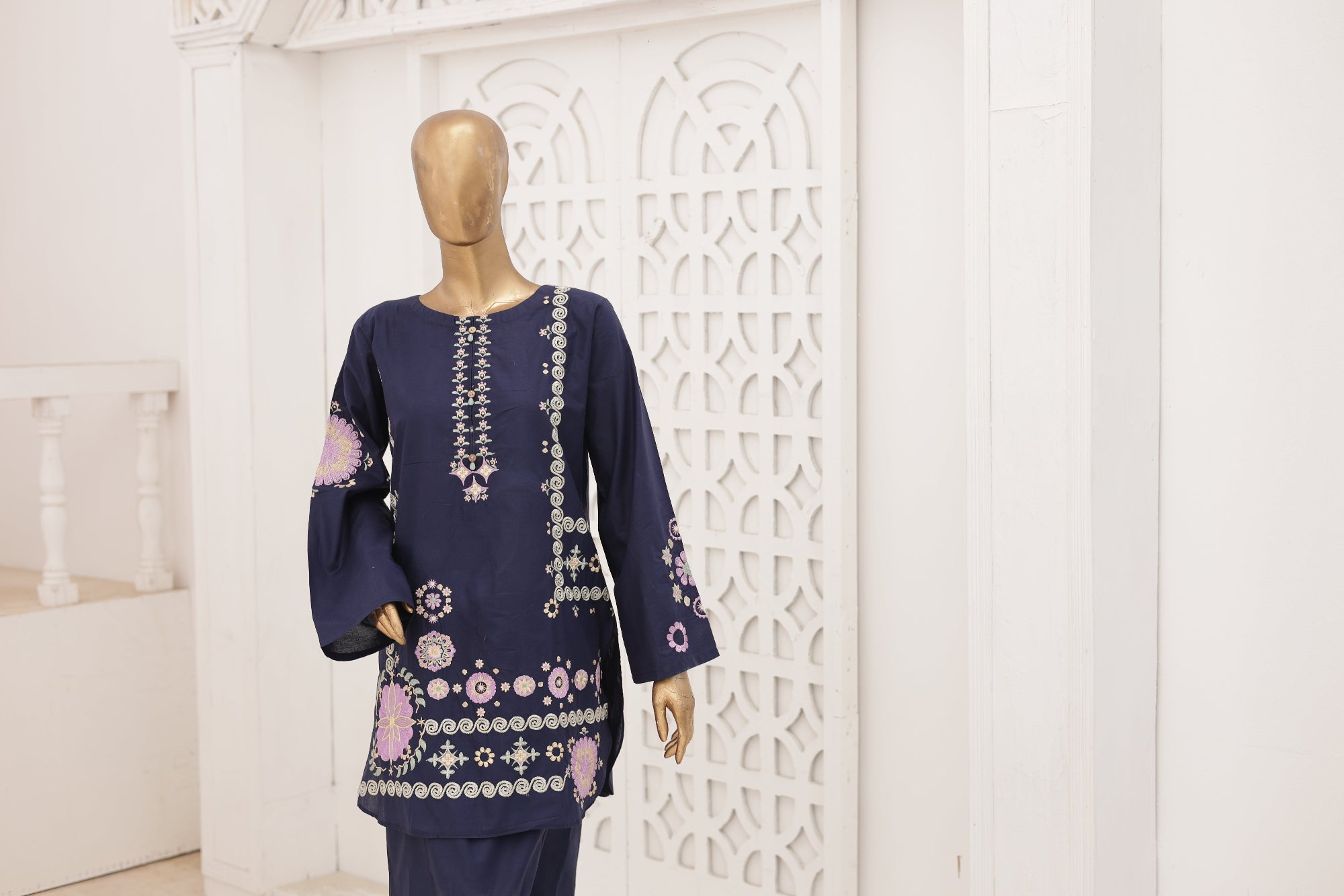 Navy blue embroidered outfit on a mannequin against a white decorative wall.