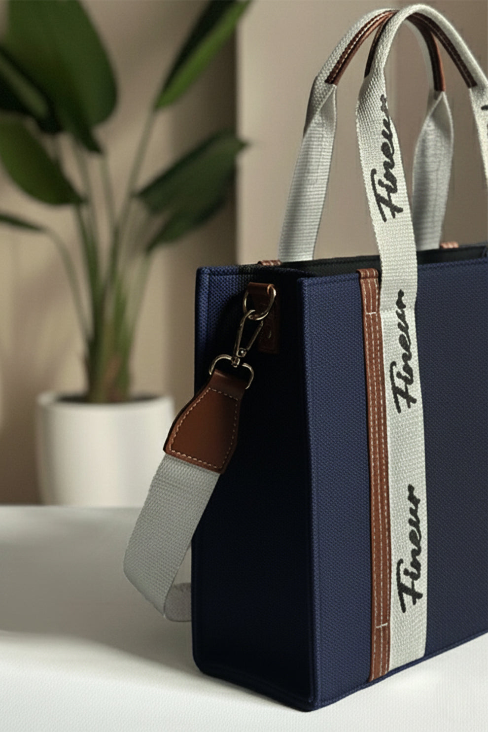 Navy Blue Tote with a white strap featuring 'fineur' branding, placed on a surface with a plant in the background.