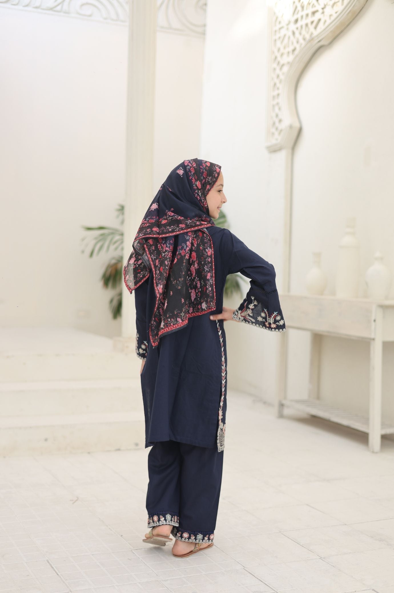Woman in a navy blue traditional outfit with a floral headscarf in a white room.