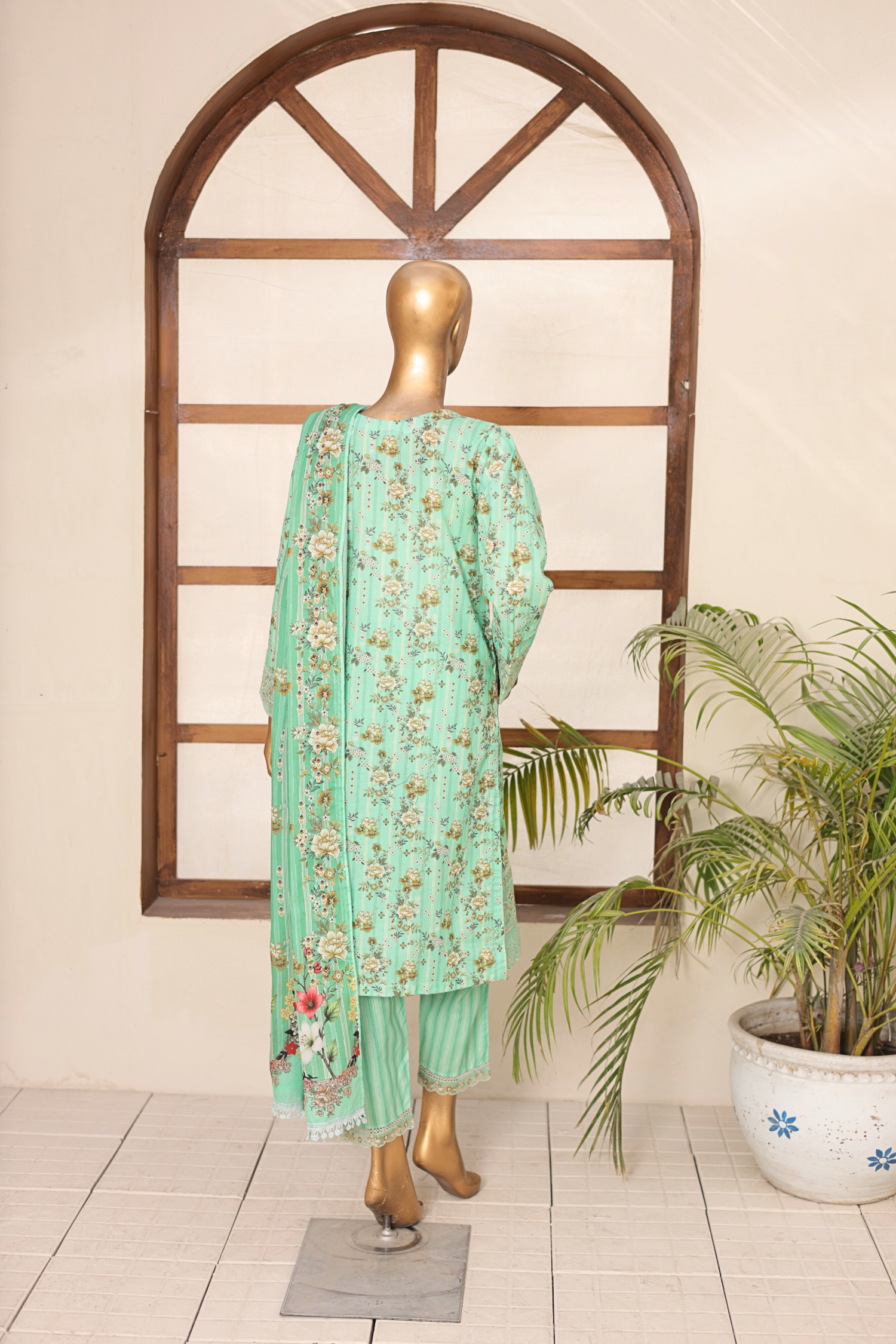 Mannequin wearing a light green embroidered outfit with a plant in the background