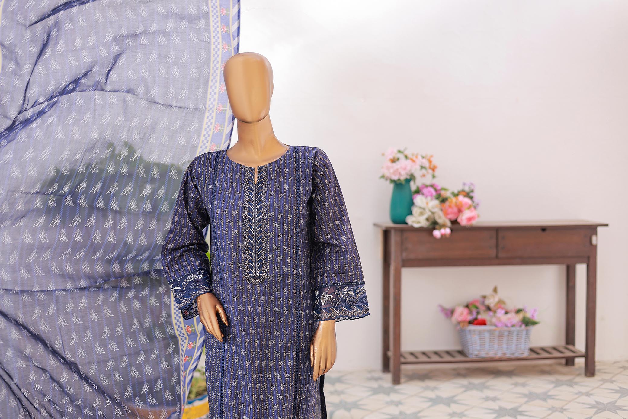 Mannequin wearing a blue patterned dress with a large fabric swatch and flowers in the background.