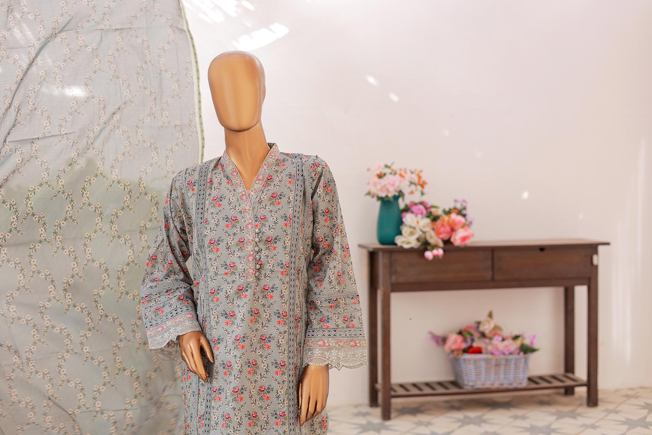 Mannequin wearing a floral dress with a decorative table and flowers in the background