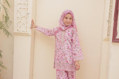 Child wearing a pink floral outfit with a matching hijab indoors.