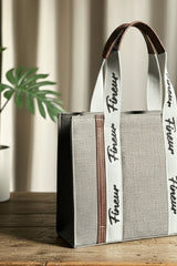 Gray Tote with a white strap featuring 'fineur' branding, placed on a surface with a plant in the background.