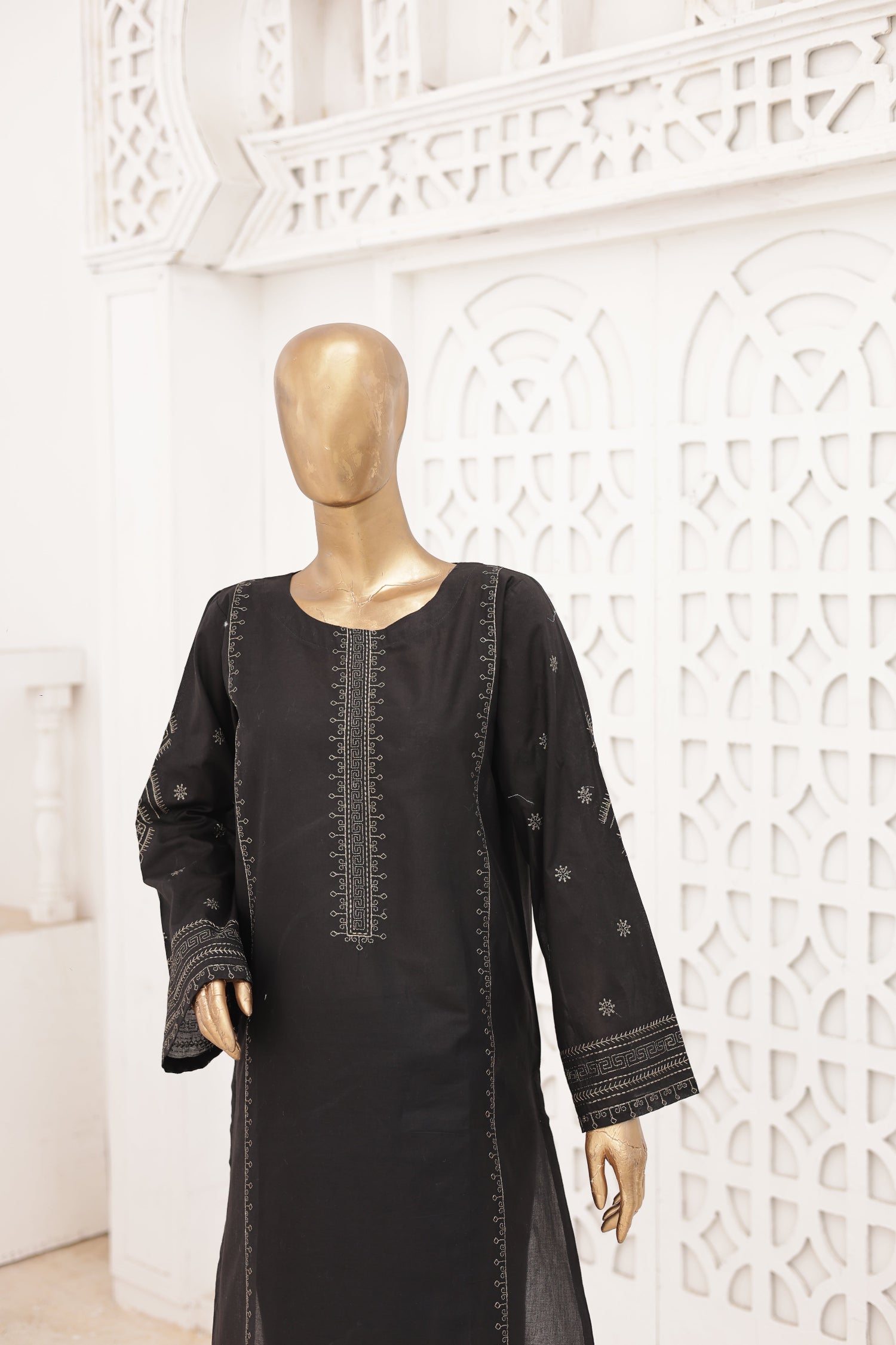 Black dress with intricate embroidery on a mannequin against a decorative white wall.