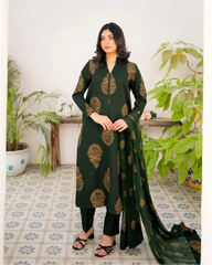 Woman wearing a bottle green traditional three piece suit with gold patterns in a room with plants.