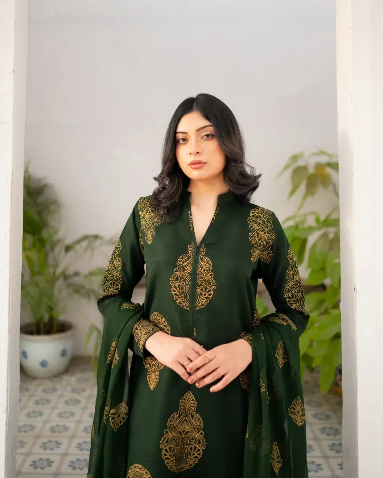 Woman wearing a bottle green dress with gold screen print in an indoor setting with plants.