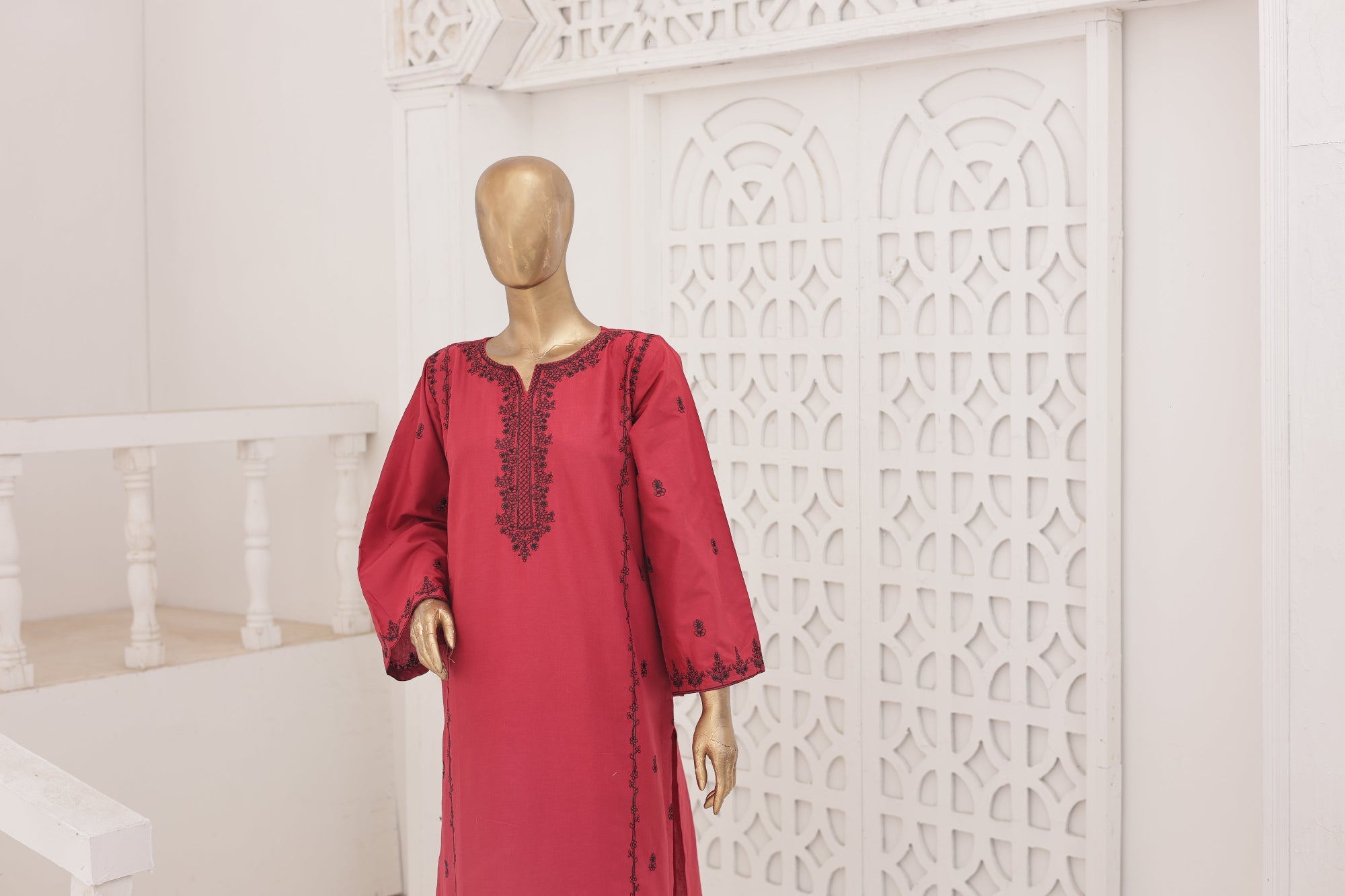 Red dress with black embroidery on a mannequin against a white decorative wall.