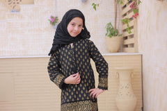 Young girl wearing a black and gold patterned outfit with a hijab in a room with decorative elements.
