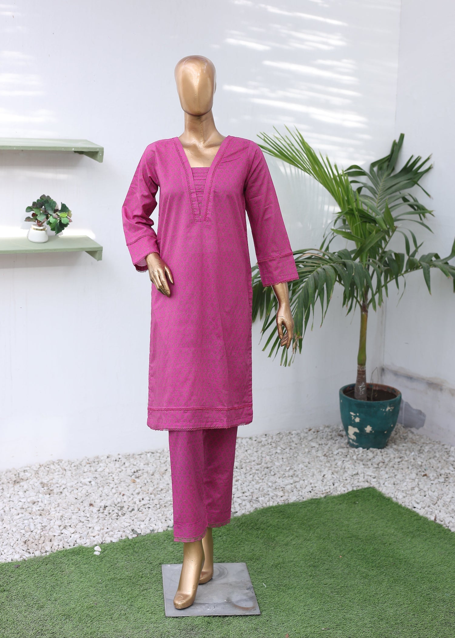 Mannequin wearing a pink outfit with a plant on a white floor.