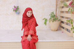 Person wearing a red traditional outfit with a matching headscarf, sitting on a white bench.