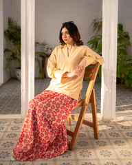 Woman sitting on a wooden chair in a sunlit room with plants and tiled floor.