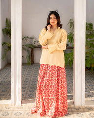 Woman wearing a lemon yellow top and red floral skirt standing in a room with plants.