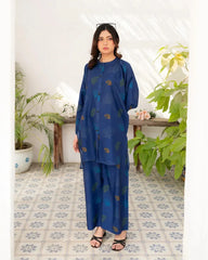 Woman wearing a navy blue outfit with leaf patterns in a room with plants and a tiled floor.