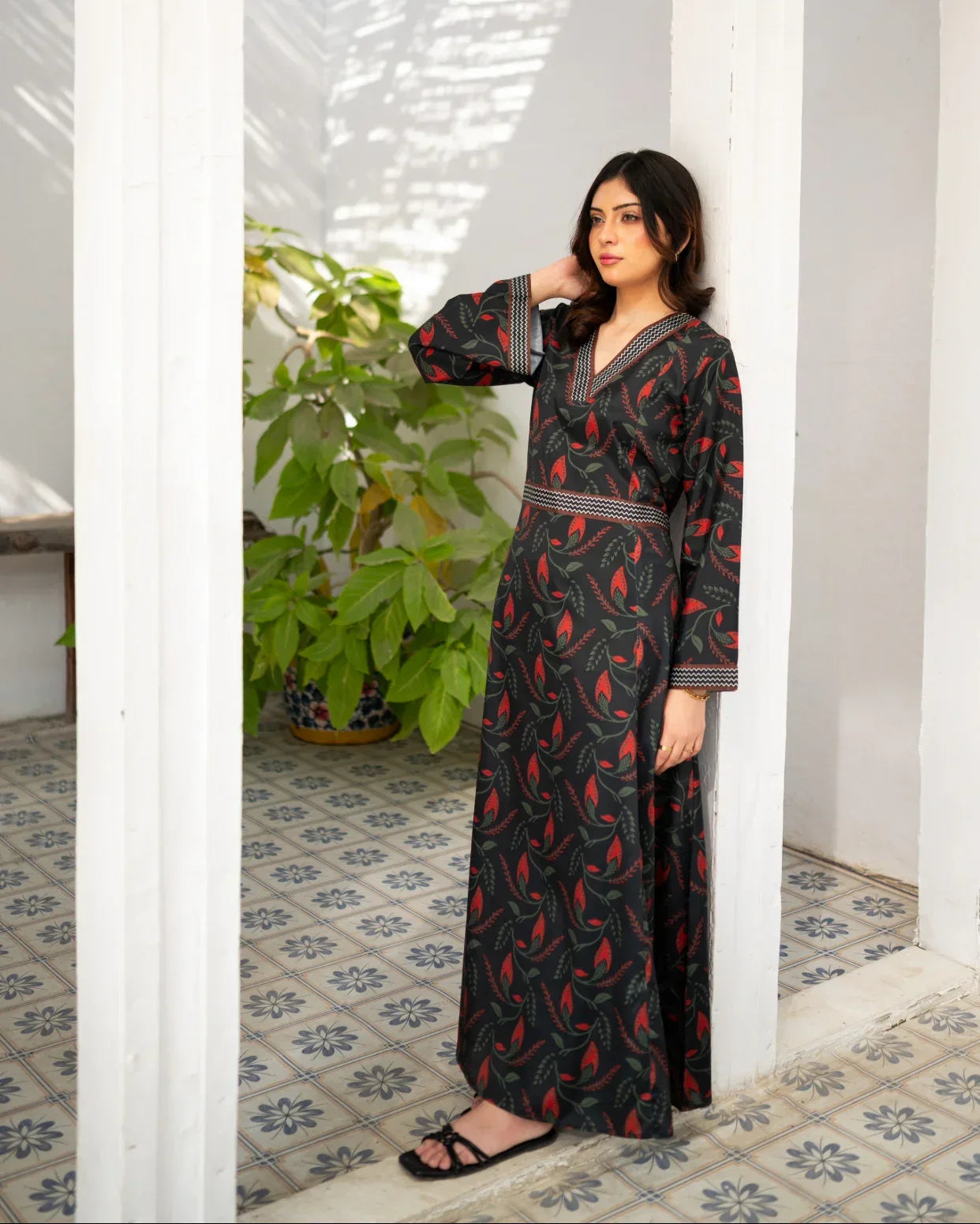 Woman wearing a black printed dress standing in a room with white walls and a tiled floor.