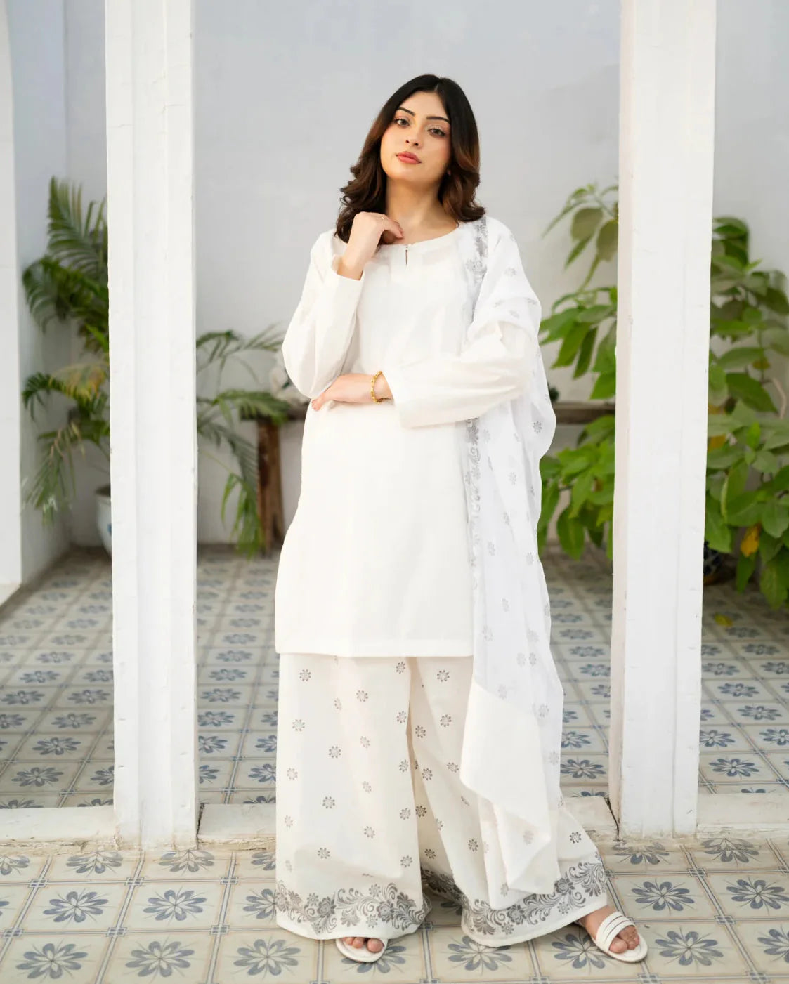 Woman in a white traditional kurta set standing in a decorative interior setting with plants.